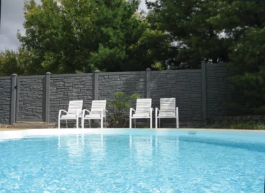 backyard pool in front of gray privacy fence with stone texture