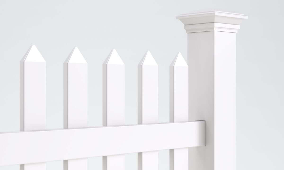 A close-up of a white picket fence with pointed tops and a decorative square post against a plain, light background.