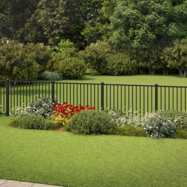 A black metal fence borders a lush green lawn with neatly trimmed bushes, white and red flowers, and trees in the background under bright daylight.