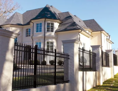 Black aluminum picket fence with stone pillars around home
